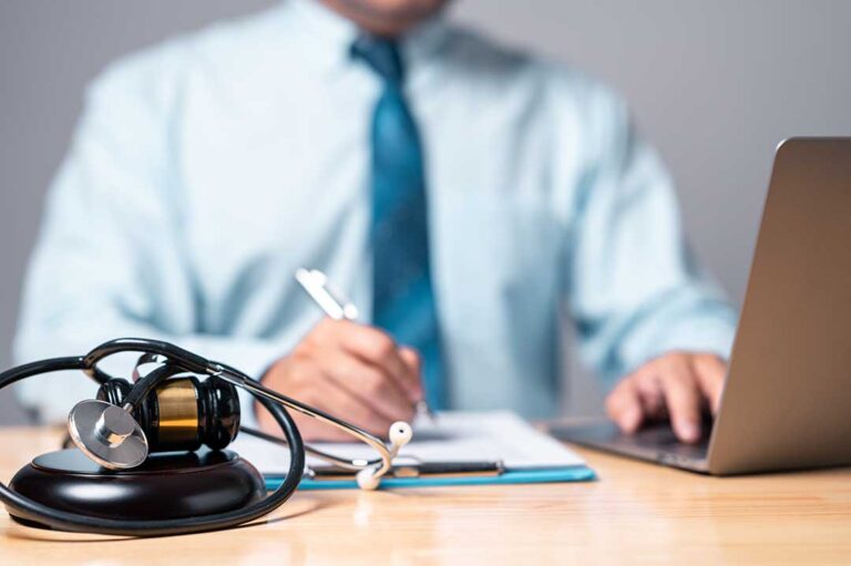 A person reviewing medical records and court papers at a desk beside a laptop and notebook.